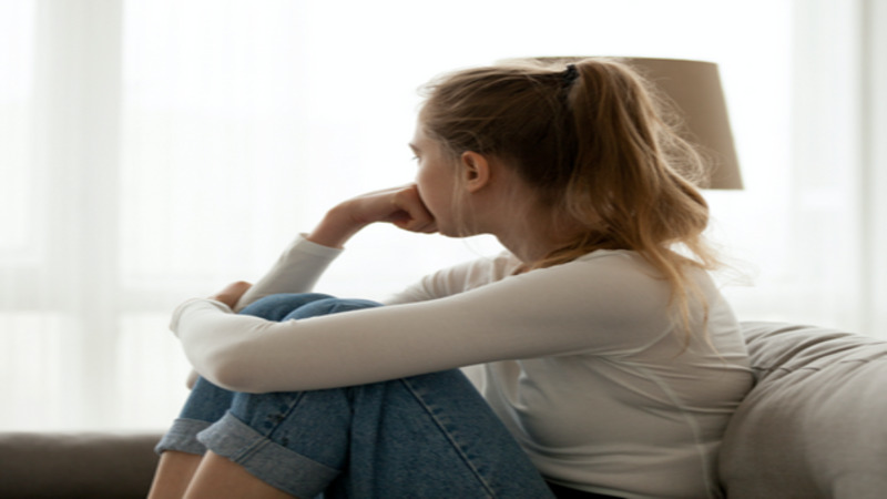 Young blonde white female sitting looking outside the window.